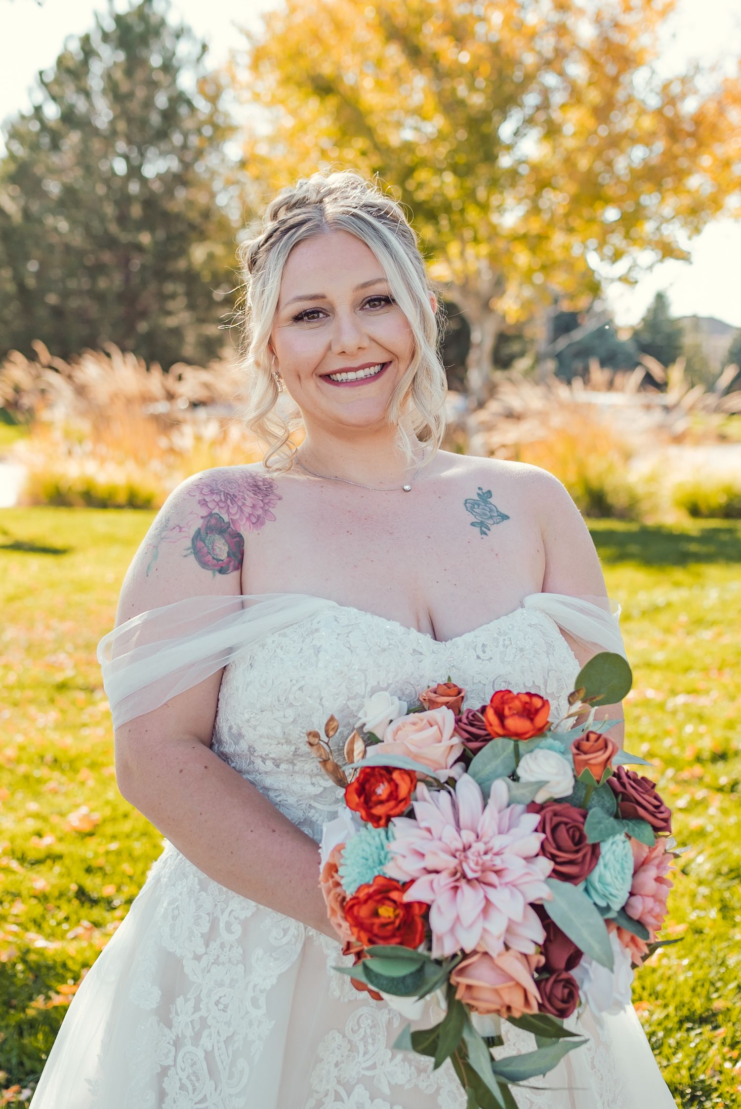 Beautiful autumn wedding photograph featuring a white lace dress and vibrant coral and pink bridal bouquet in a garden setting.