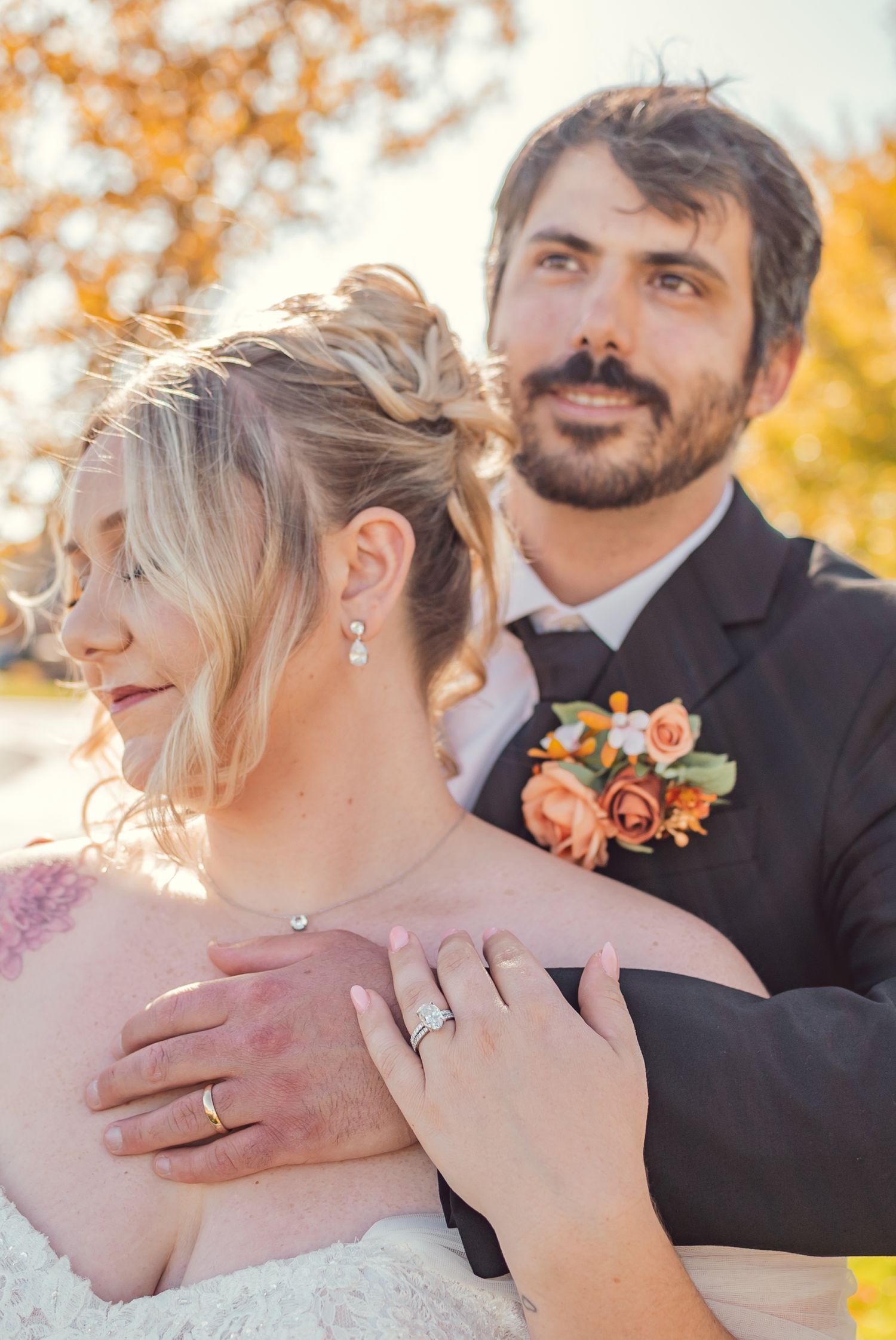 A romantic wedding photo captured outdoors in autumn with orange and pink florals and warm fall colors in the background.