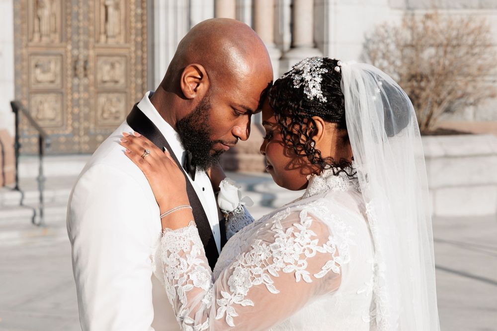 Bride and groom sharing an intimate forehead-to-forehead moment outside a grand stone church.