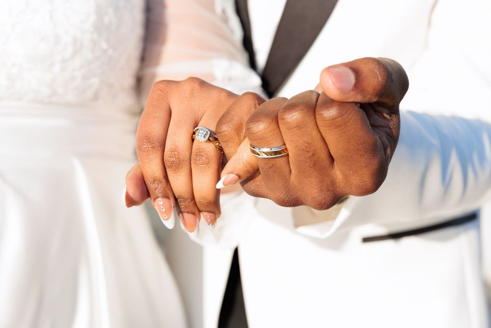 Close-up of newlyweds hands showing wedding rings, bride with white manicure and groom in white suit.