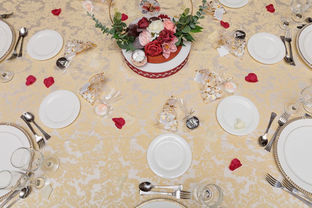 Elegant wedding reception table set with gold damask linens, white plates, and red rose centerpiece.