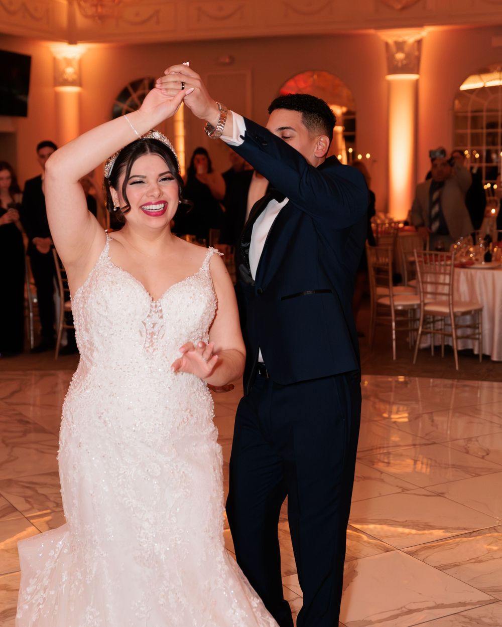 Bride in beaded mermaid gown dancing with groom in navy tuxedo at wedding reception.