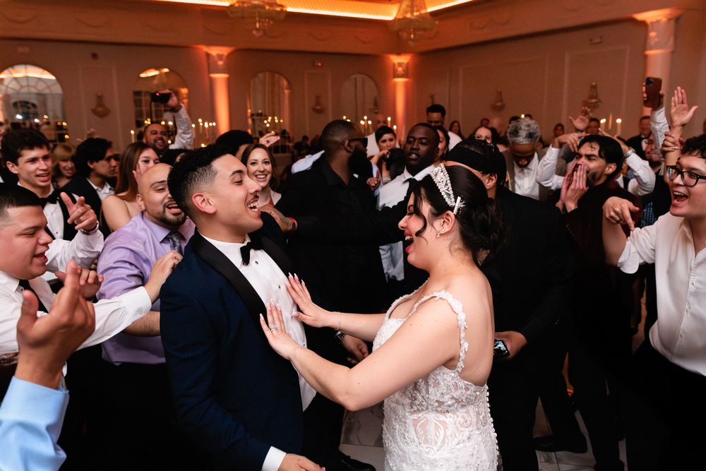 Bride and groom share a joyful first dance surrounded by cheering guests at an elegant wedding reception.