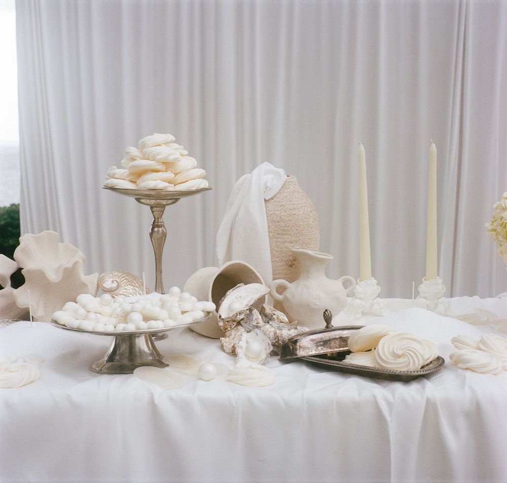 Elegant white wedding table setting with candles, cake stands, and seashell decorations on a white tablecloth.