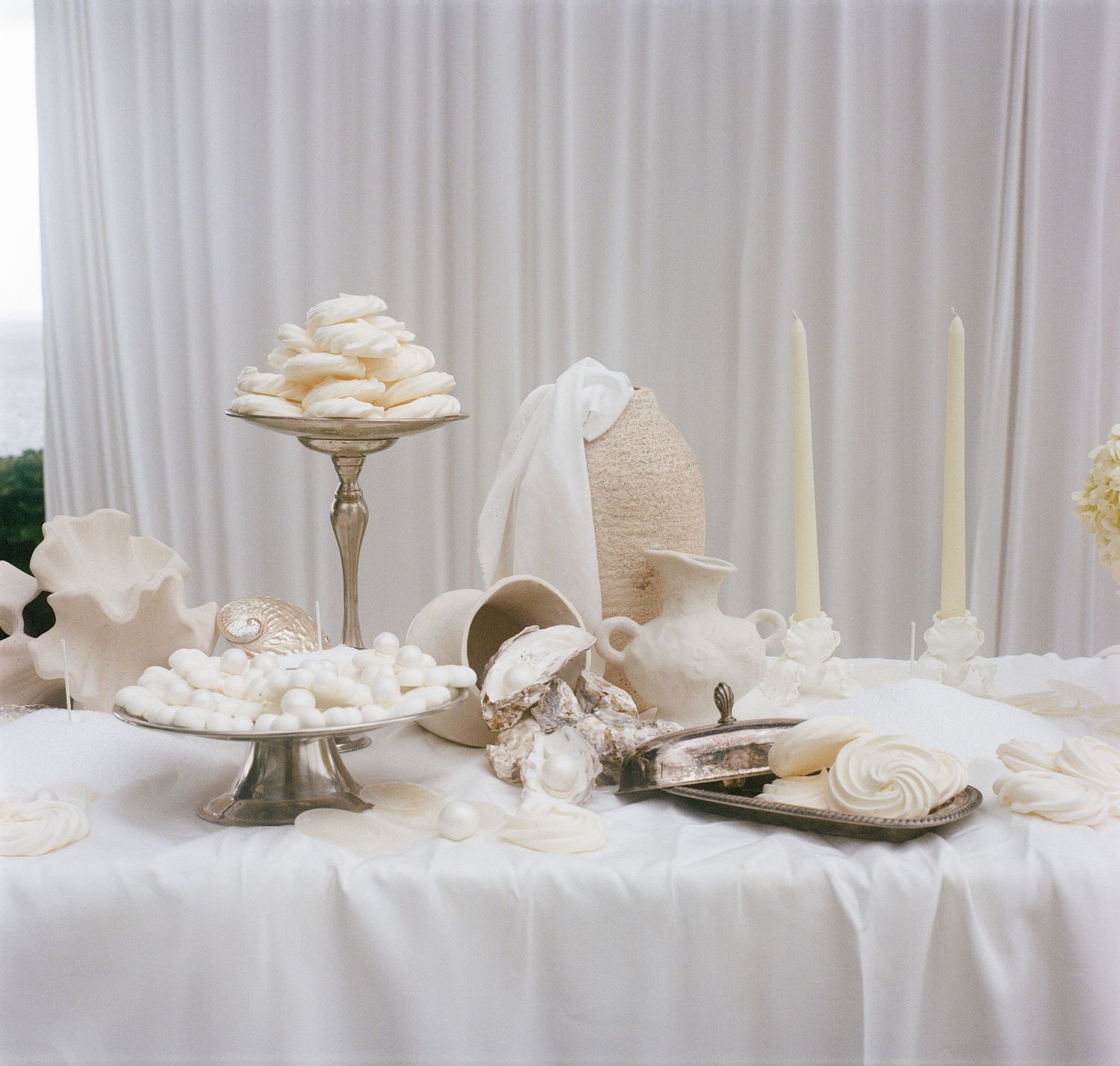 Elegant white wedding table setting with candles, cake stands, and seashell decorations on a white tablecloth.
