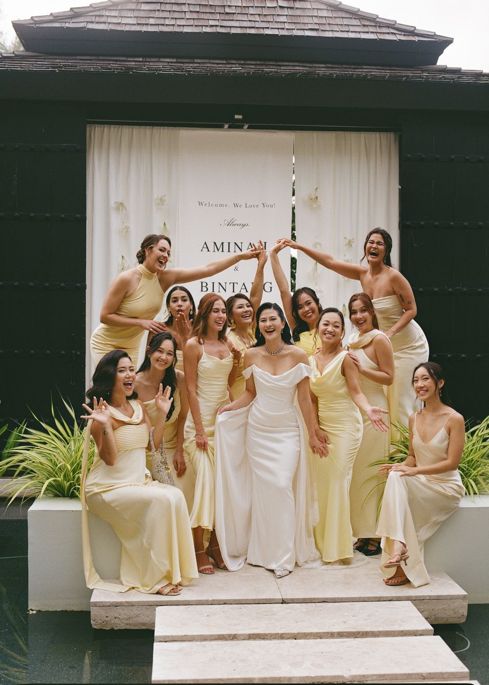 Wedding party in elegant cream and white dresses posing on steps of building.