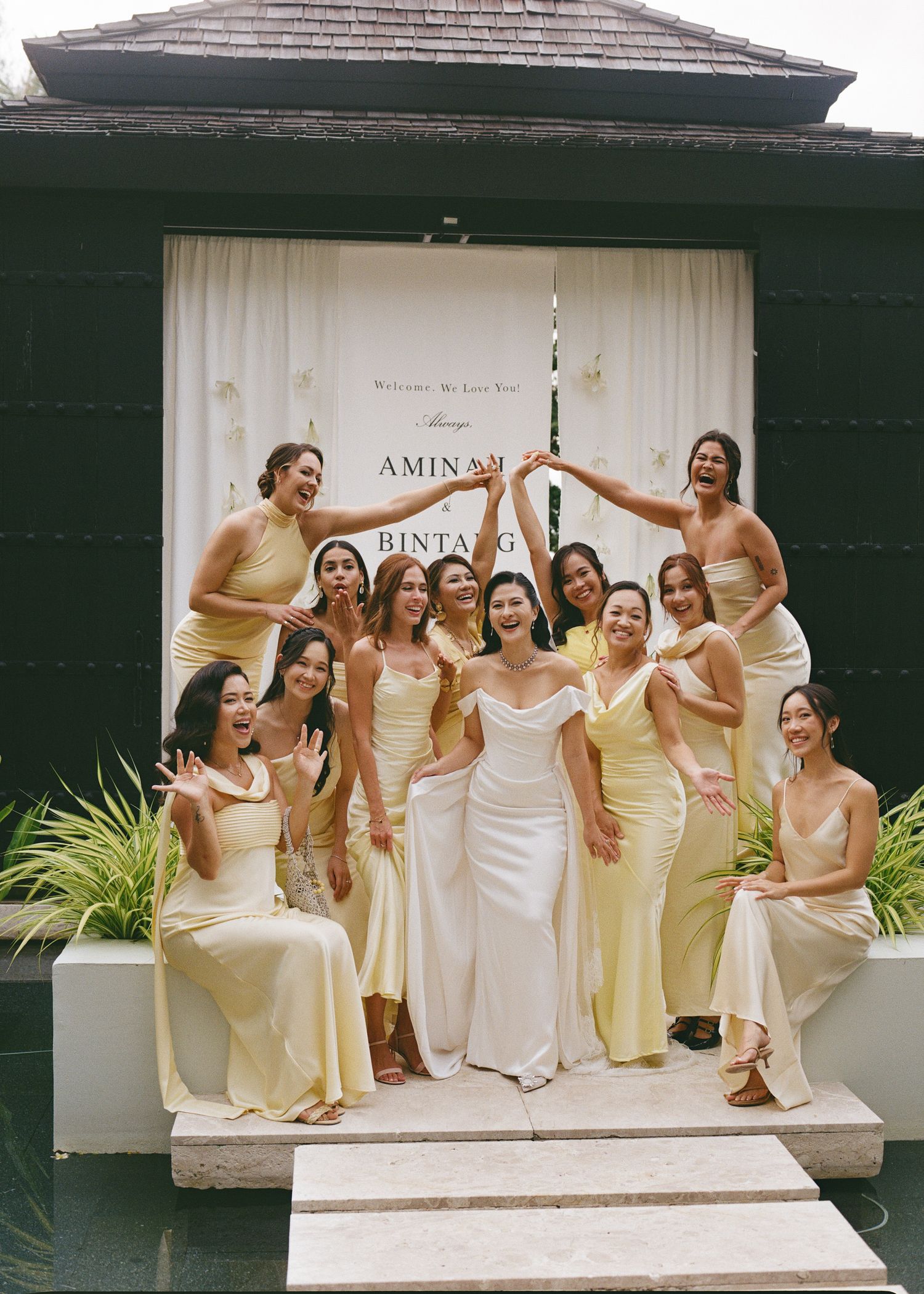 Wedding party in elegant cream and white dresses posing on steps of building.