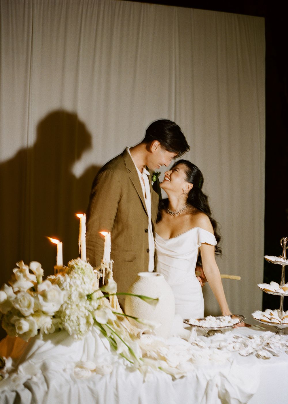 Romantic wedding table scene with white flowers, candles, and a couple sharing an intimate moment.