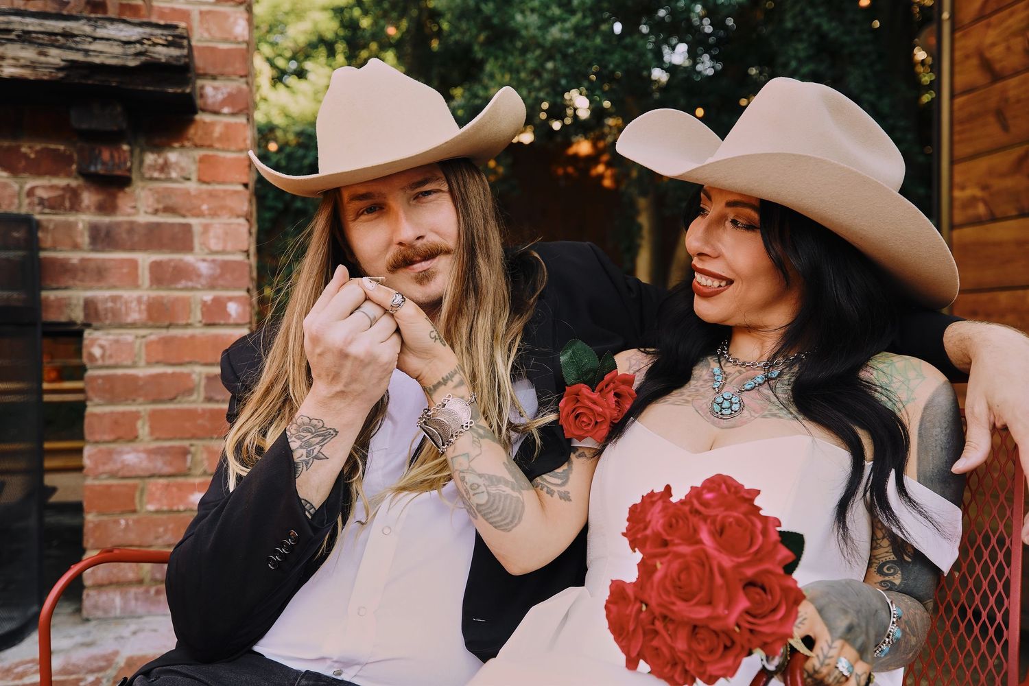 Two people in western attire sharing a romantic moment against a brick wall backdrop.