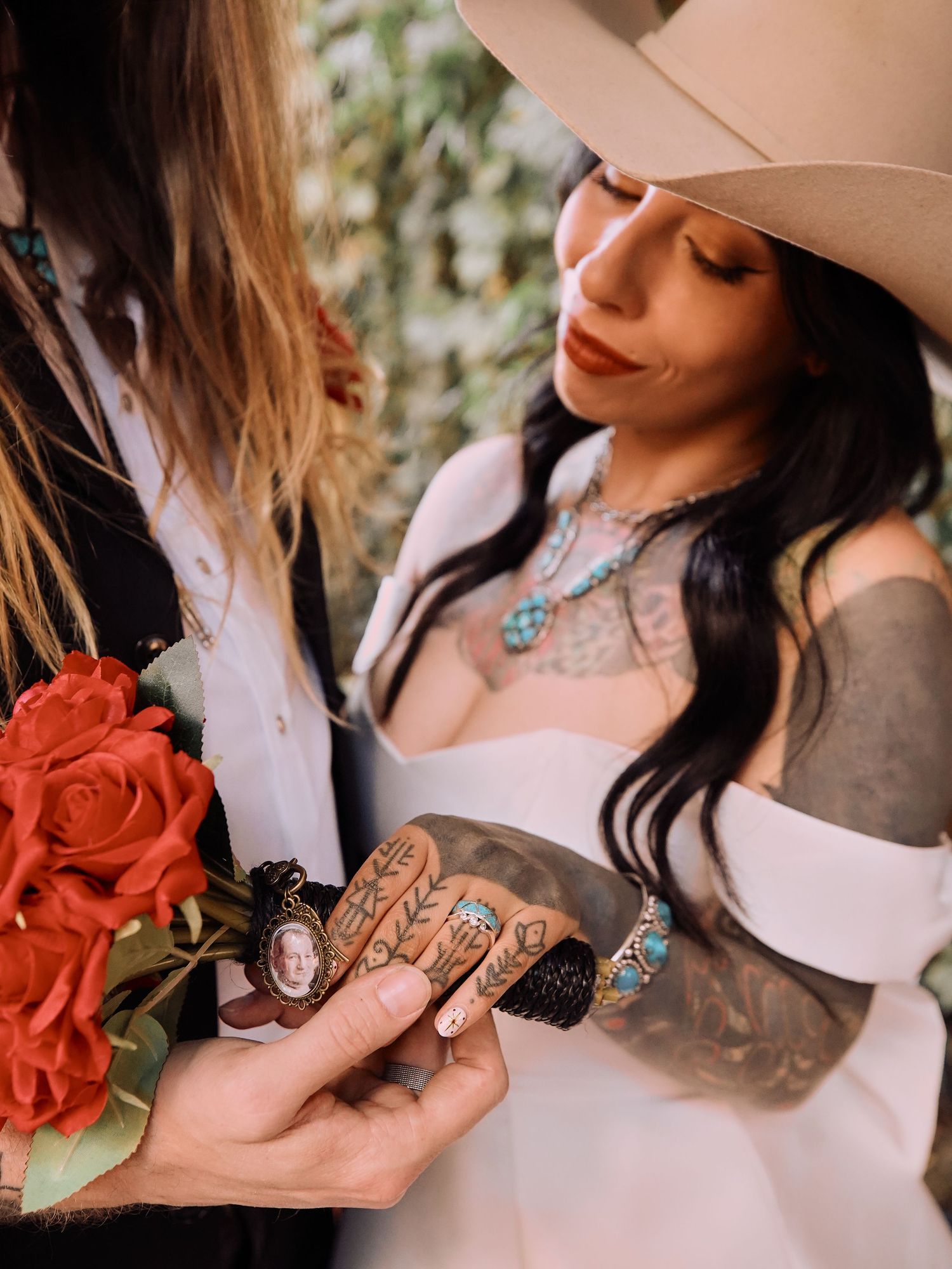 Two people in cowboy hats holding red roses and showing off wedding rings in a romantic photoshoot.