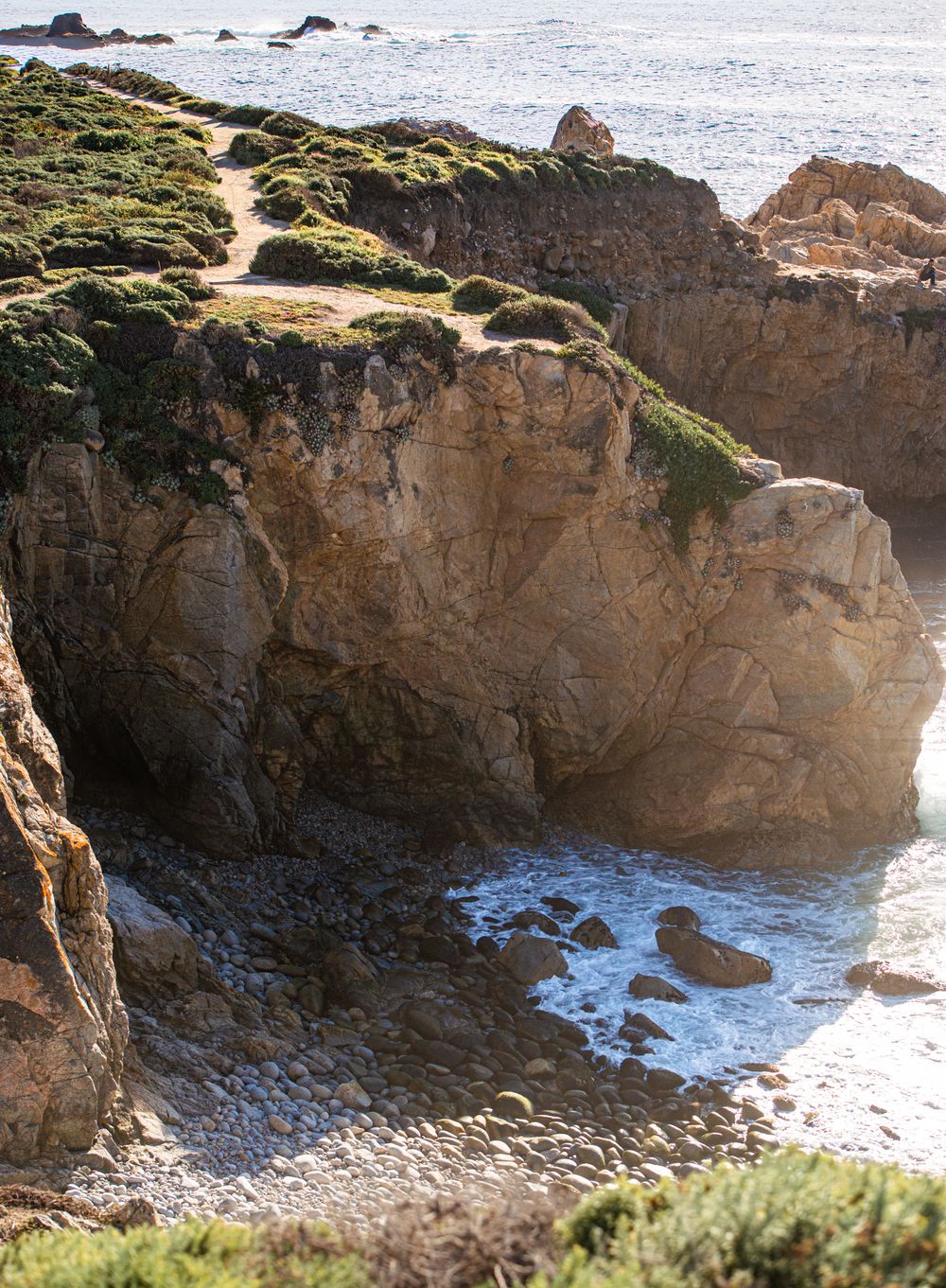 Rocky coastal cliffs with green moss overlooking a small secluded cove with gentle waves on a sunny day.