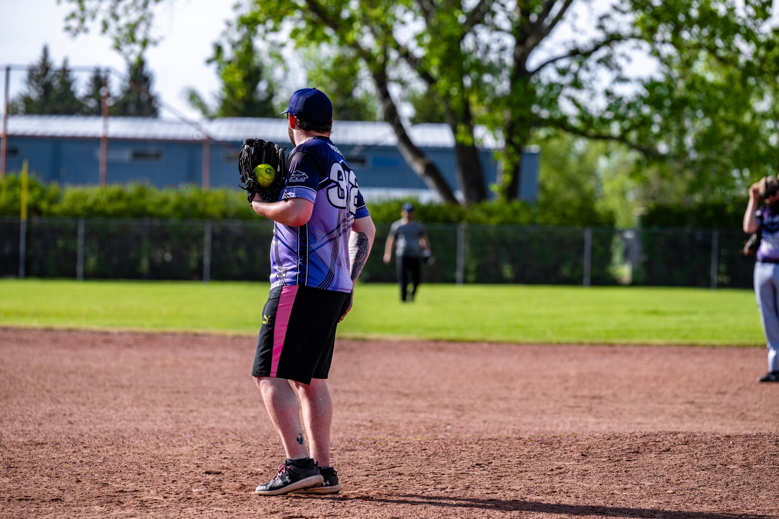Youth baseball player in blue uniform stands ready on the dirt infield during a game.
