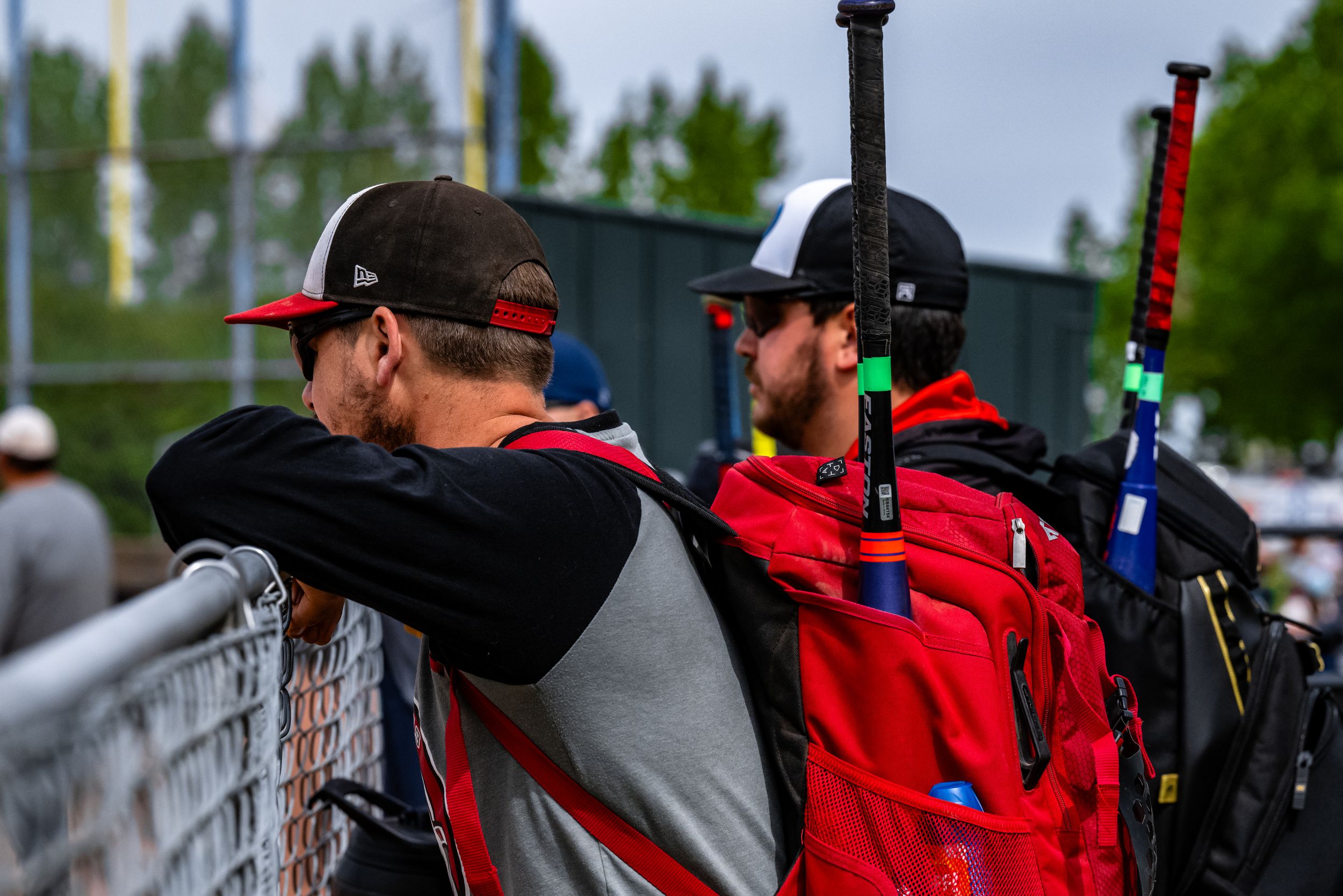 Baseball players in red uniforms watch from dugout during game while holding baseball bats.