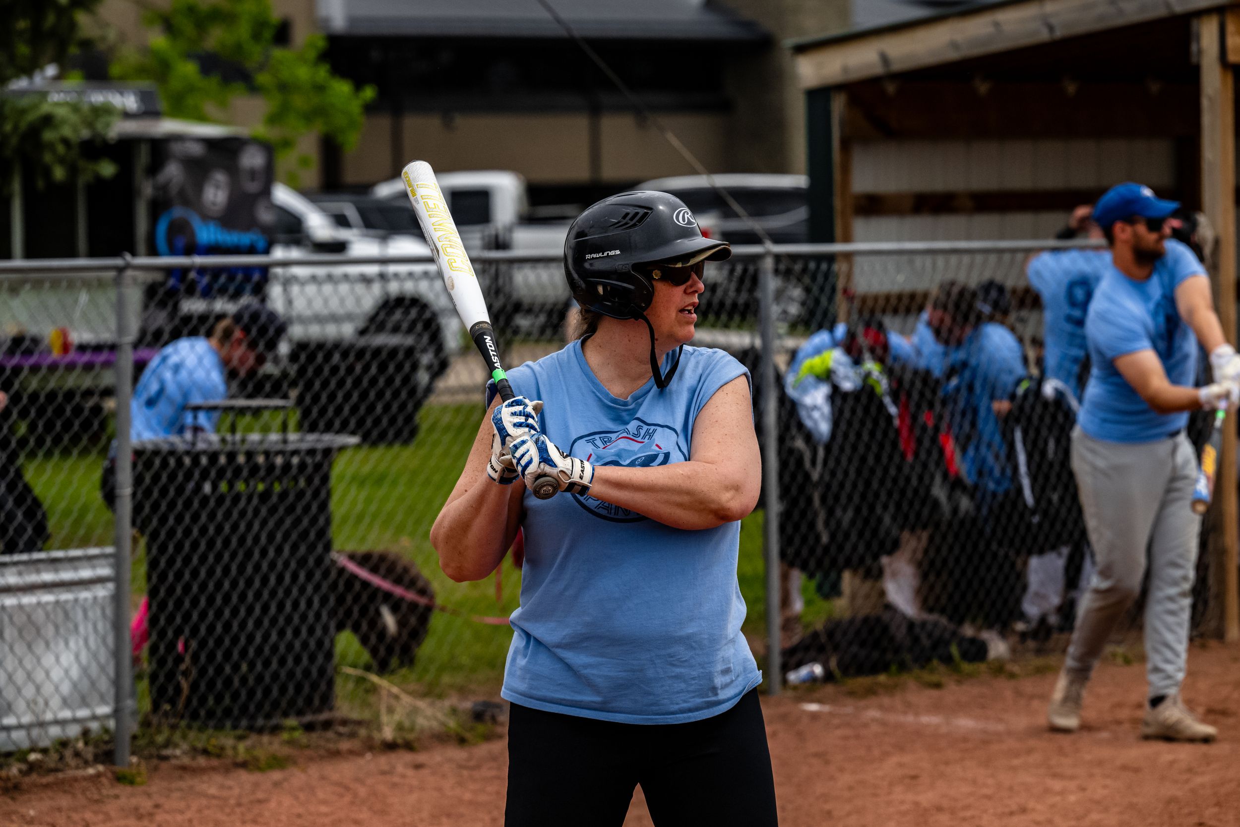 Baseball players in light blue uniforms gather on a field during a game near a chain link fence.