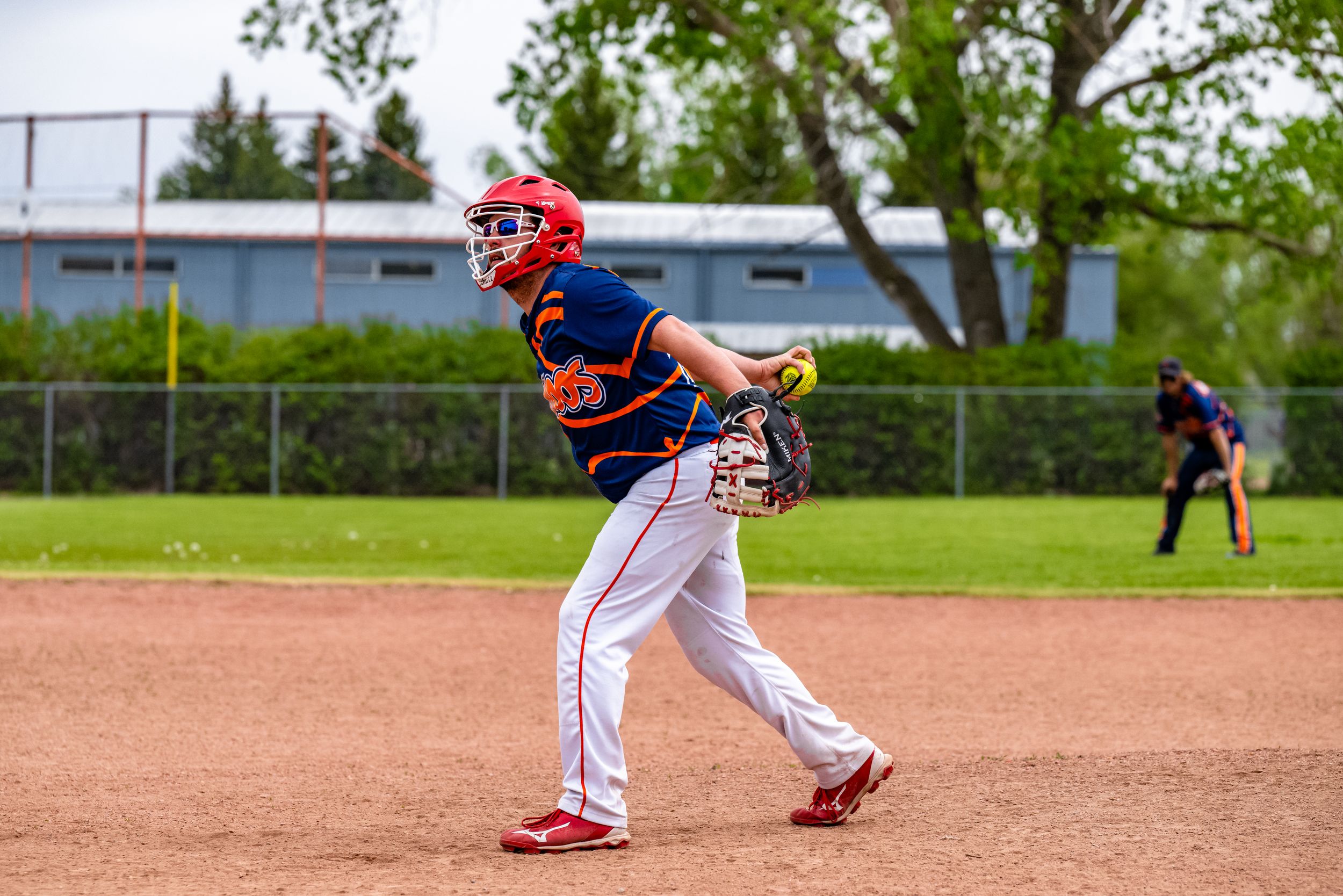 Youth baseball players in red uniforms practicing batting and fielding skills on a sunny day at a baseball diamond.