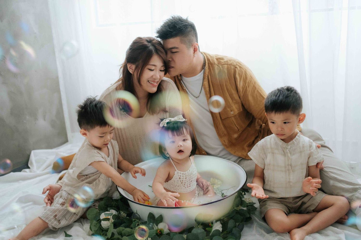 A baby sits in a white chair surrounded by floral decorations and balloons at a birthday celebration.