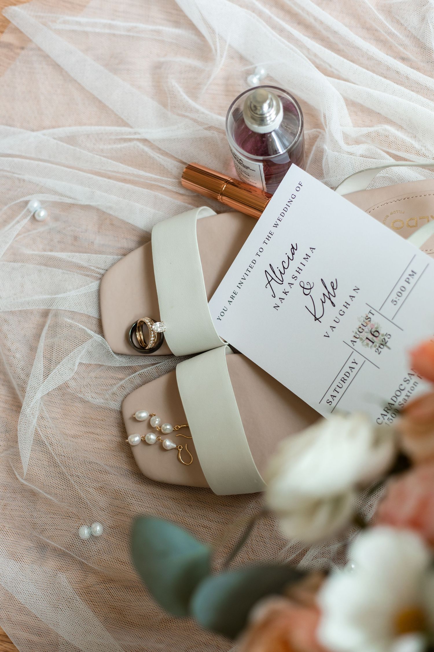 Elegant wedding details featuring cream shoes, perfume bottle, cinnamon sticks and invitation on soft fabric background.