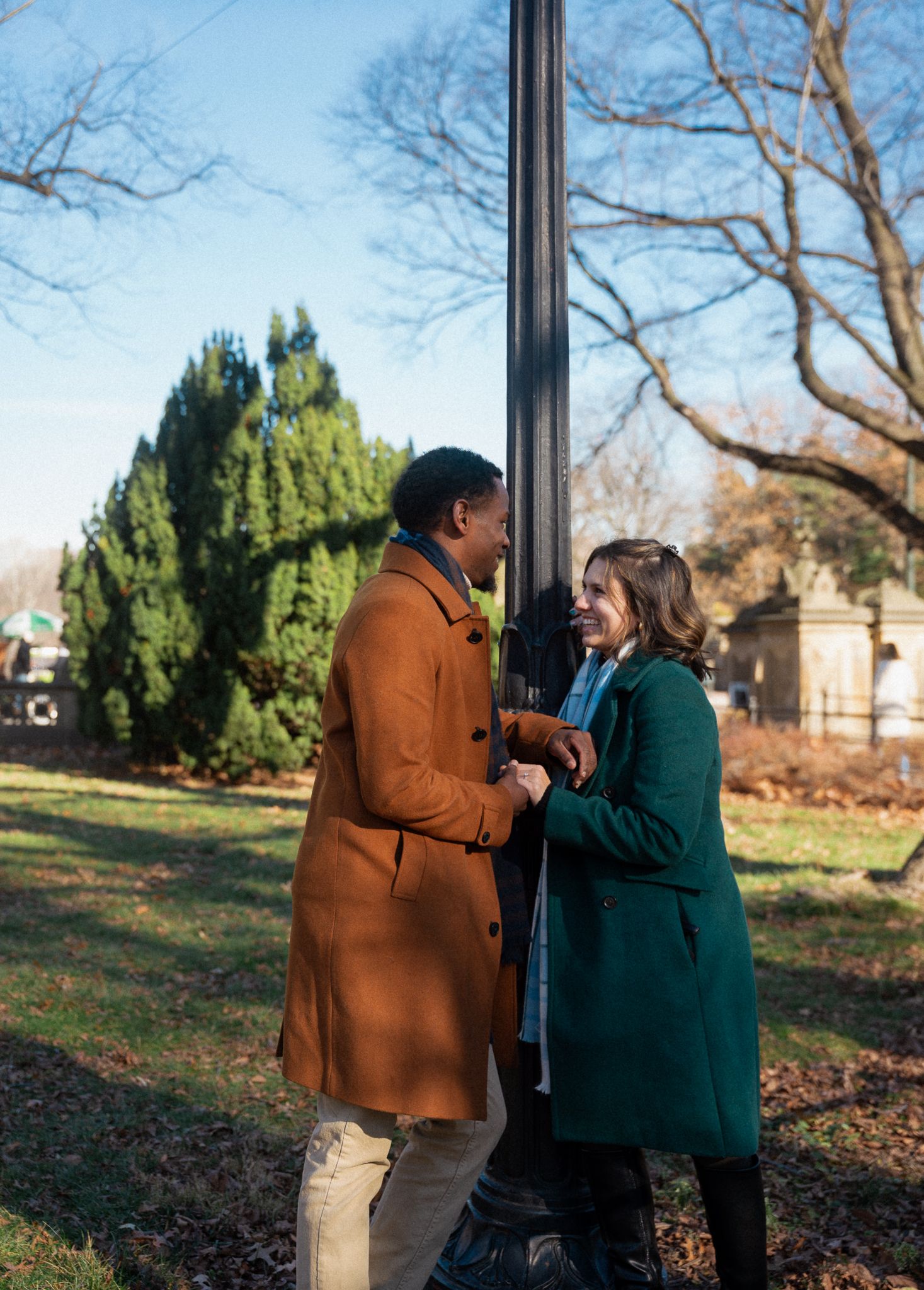 A couple sharing an intimate moment by a lamp post in a park during autumn.