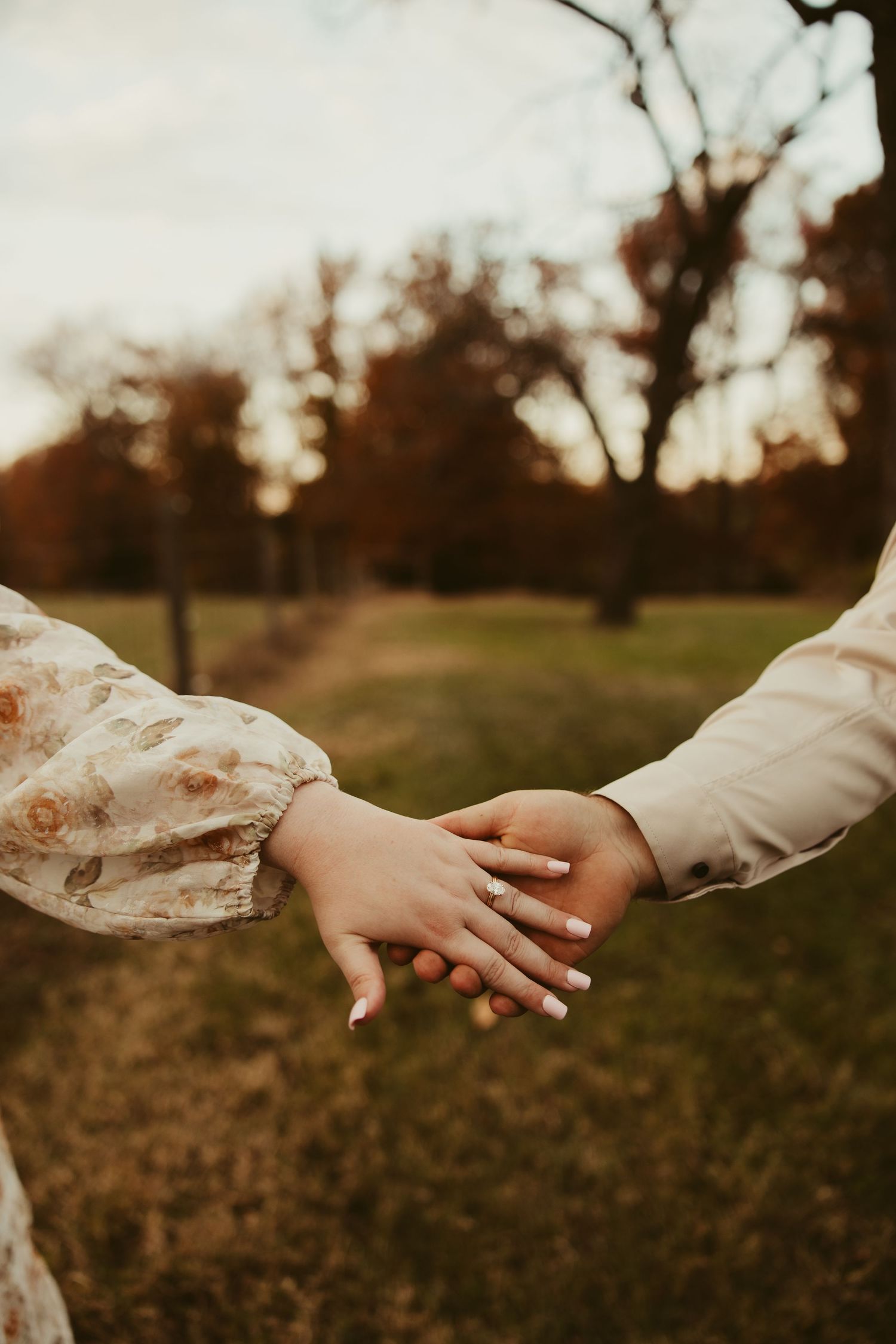 Close-up of couple holding hands with engagement ring in autumn park.