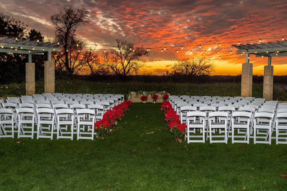 Rows of white wedding chairs set up on a lawn with pillars and a dramatic orange sunset sky in the background.