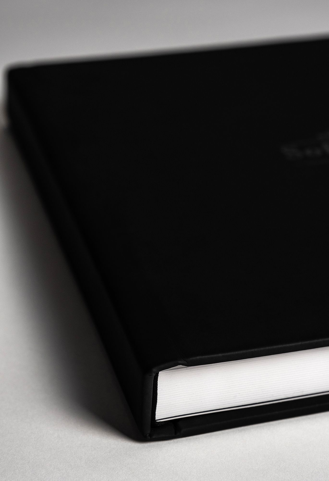 Close-up view of a black hardcover book or notebook with white pages visible from the side against a light background.