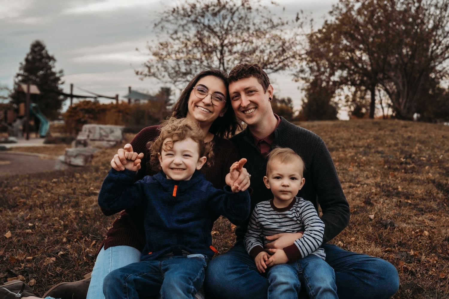 Family gathered outdoors on grassy hill during fall season photoshoot.