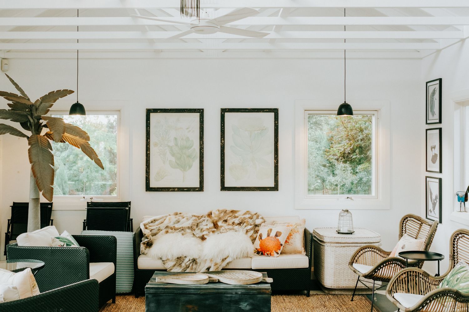 Minimalist living room with white walls features framed artwork, plants, and modern furniture in neutral tones.