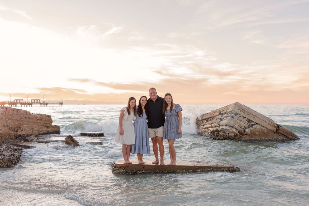 Coastal family portraits with crashing waves and dramatic sunset sky.