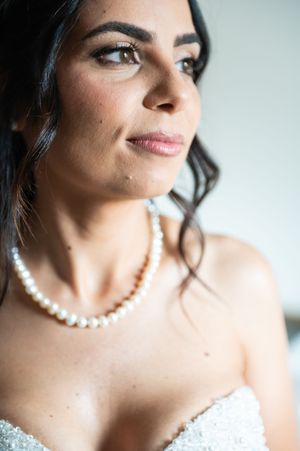 Close-up details of a pearl necklace and white lace dress against a soft light background.