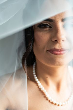 Close-up artistic portrait of someone wearing a delicate veil and elegant pearl necklace in soft lighting.