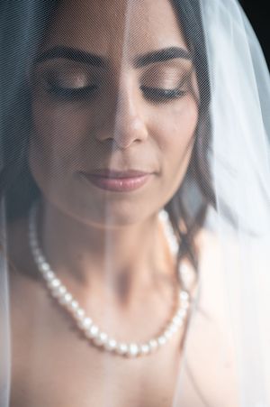 A bride wearing a delicate pearl necklace and white veil smiles with closed eyes in a series of soft, dreamy portraits.