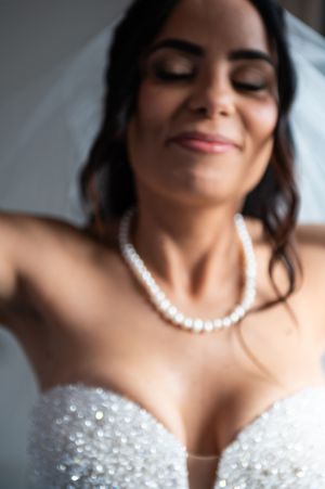 A bride wearing a pearl necklace and sparkly strapless dress smiles serenely with closed eyes.