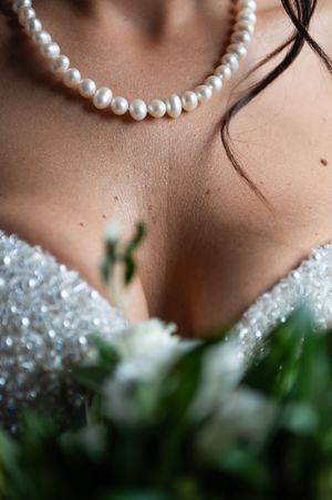 A delicate pearl necklace adorns a neckline with soft focus greenery and sparkles in the background.