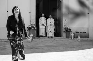A black and white photograph showing people in coats standing in a doorway with floral arrangements on either side.