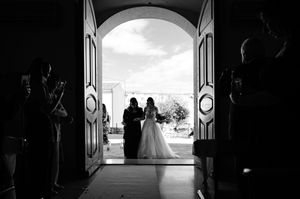Silhouetted figures stand in a bright church doorway creating a dramatic backlit wedding scene.
