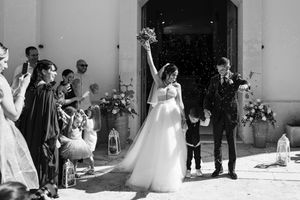 A black and white wedding photo showing newlyweds exiting a church while guests celebrate with bubbles and flowers.