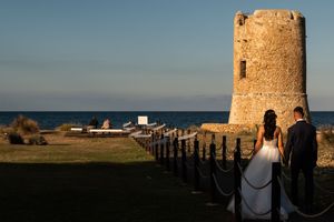 A panoramic view of a historic stone tower on a hilltop during golden hour with distant coastal landscape.