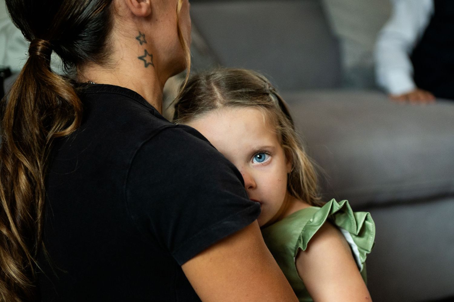 A mother and daughter share an intimate moment together on a grey couch.