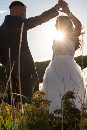 Silhouetted couple dancing in a meadow at sunset with sunburst and wildflowers in the foreground.