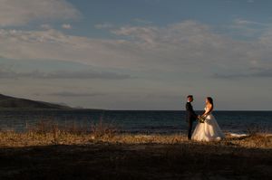Dramatic coastal landscape with couple silhouetted against ocean and mountains during golden sunset.