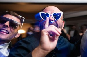 A group of people wearing sunglasses and formal attire dancing and celebrating at what appears to be a wedding reception.