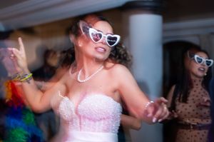 People in sunglasses and wedding attire dancing energetically at a reception with columns visible in the background.