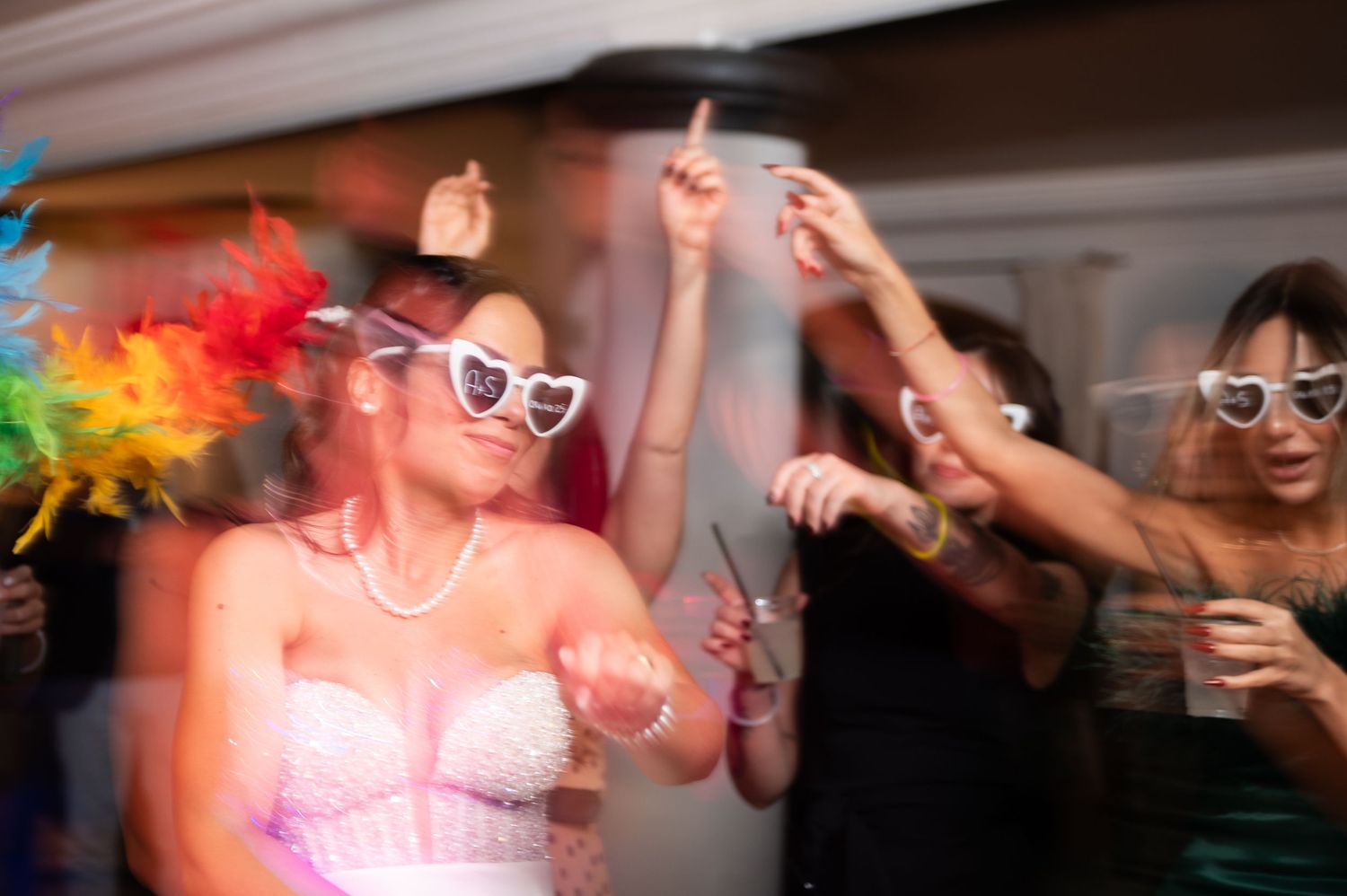 People dancing and celebrating at a lively party with colorful lights and bubbles in a dimly lit room.