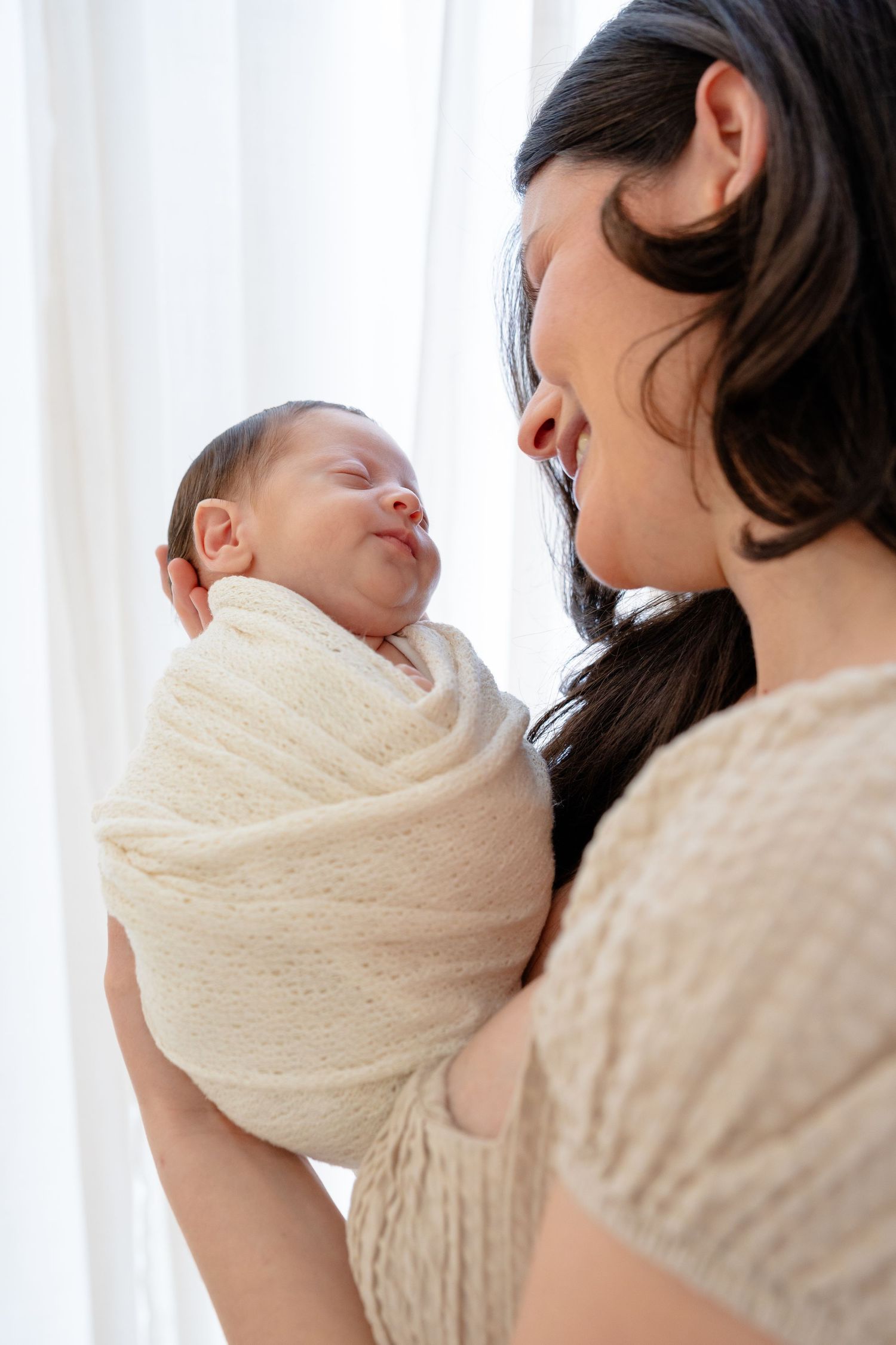 A series of photos showing a mother in black hair holding a sleeping baby wrapped in a cream-colored blanket.