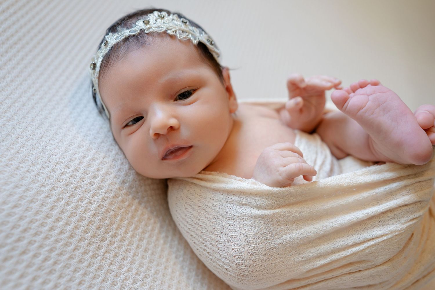 A newborn baby wrapped in a white blanket lies on a soft surface in a series of similar poses.