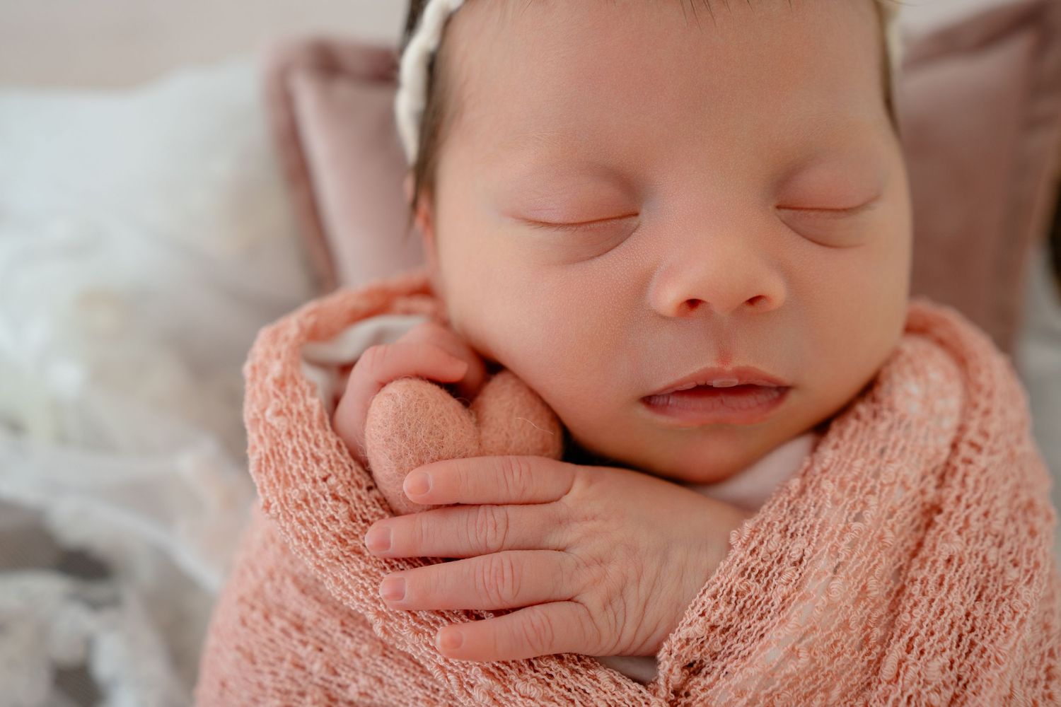 Sleeping newborn wrapped in soft pink knit blanket during peaceful professional photography session.