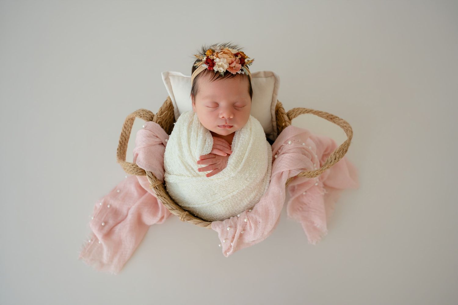 Newborn baby sleeping peacefully in neutral tones with delicate peach floral accessories.