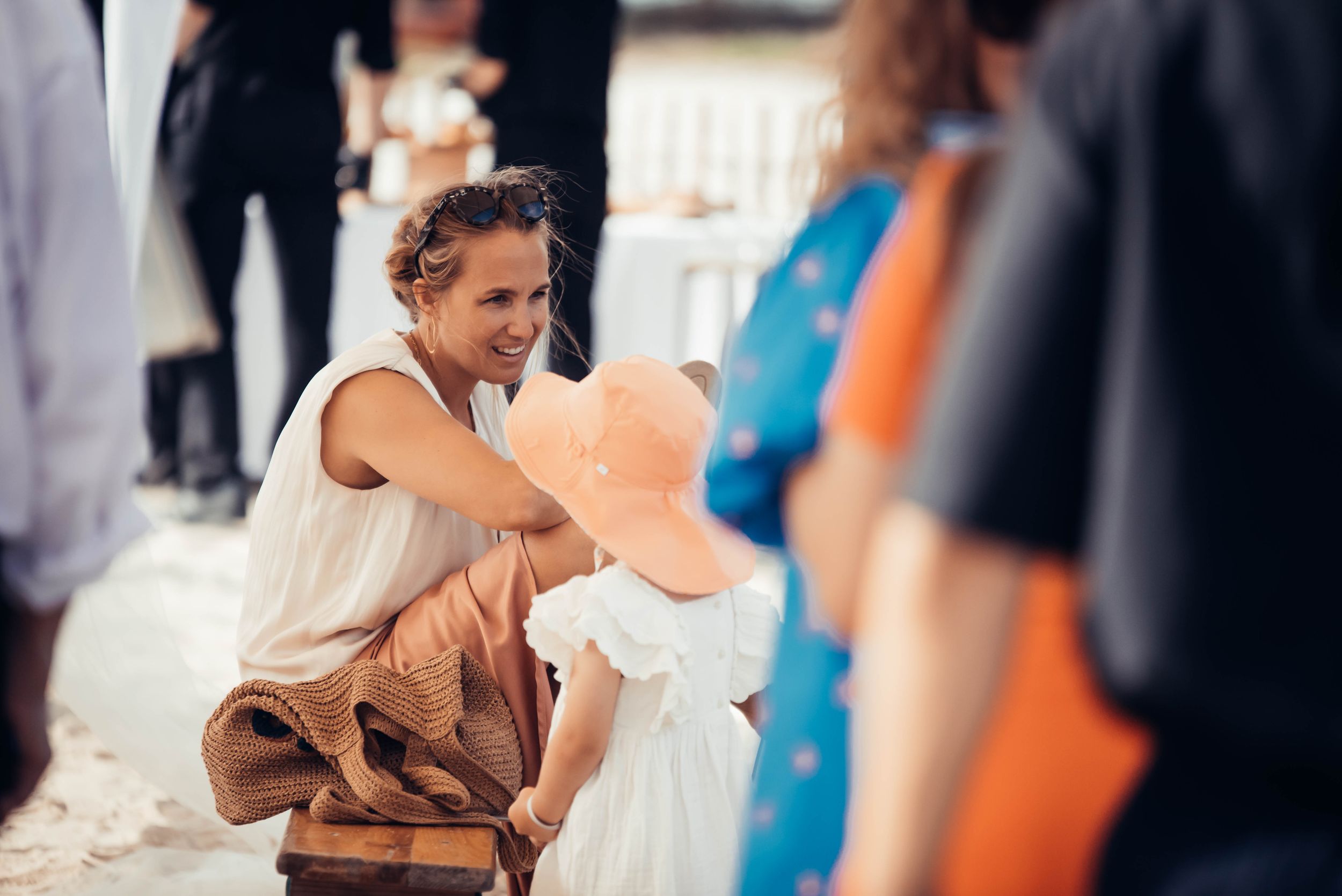 Invitée souriante assise pendant le vin d’honneur d’un mariage en extérieur sous le soleil.
