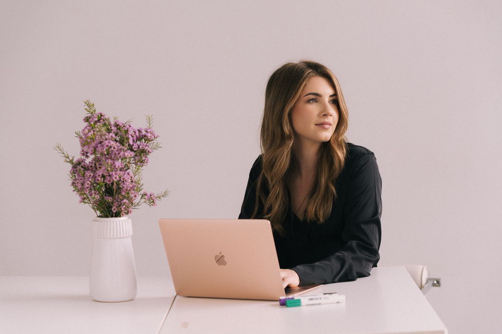 Professional workspace with laptop, floral arrangements and minimalist aesthetic in soft pink and white tones.