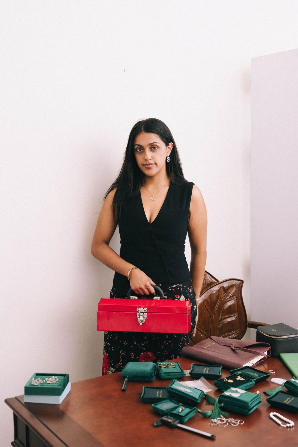 A person in black sits at a desk with jewelry and accessories spread across the surface.
